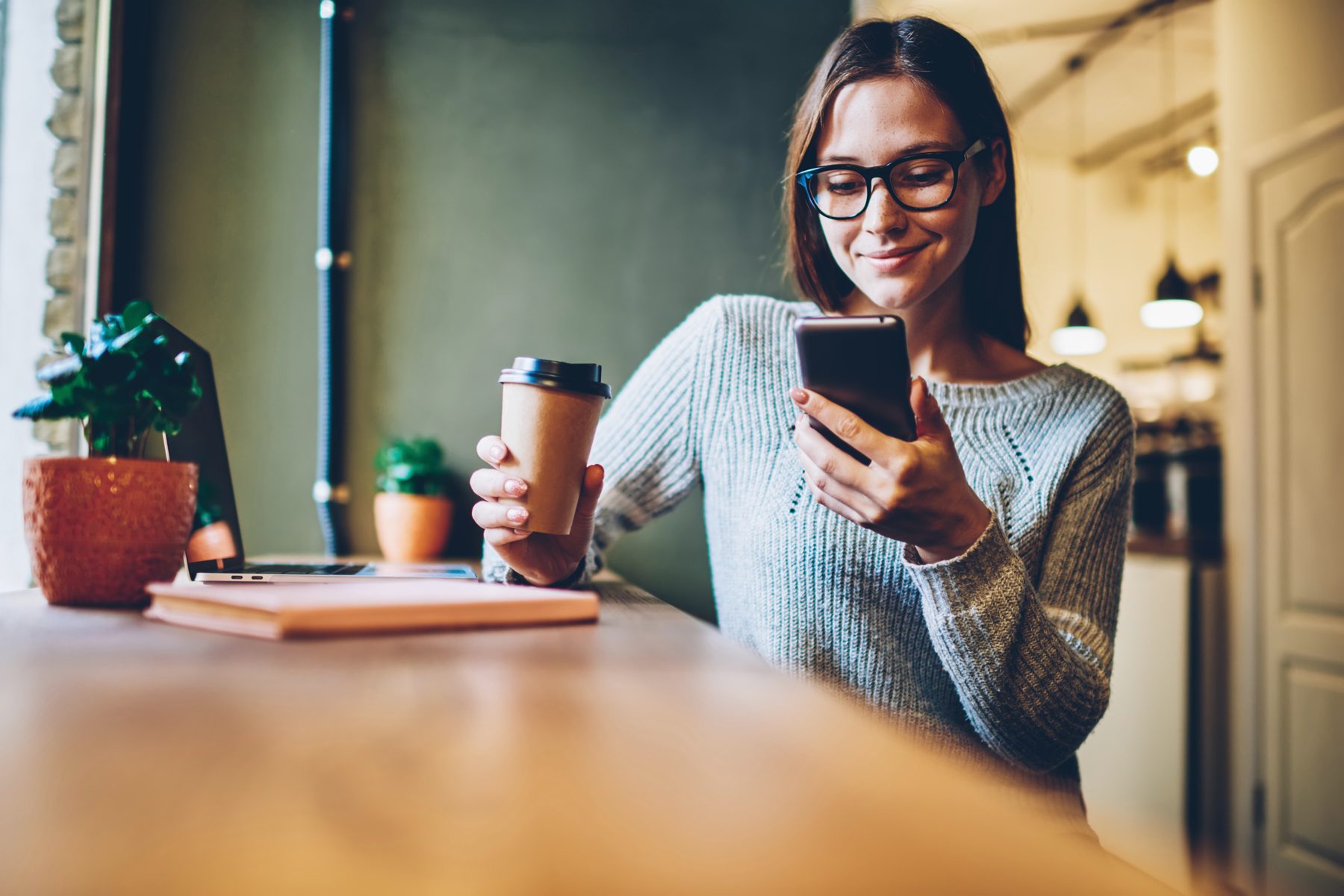 Une jeune active lit sur son téléphone avec un café dans un café