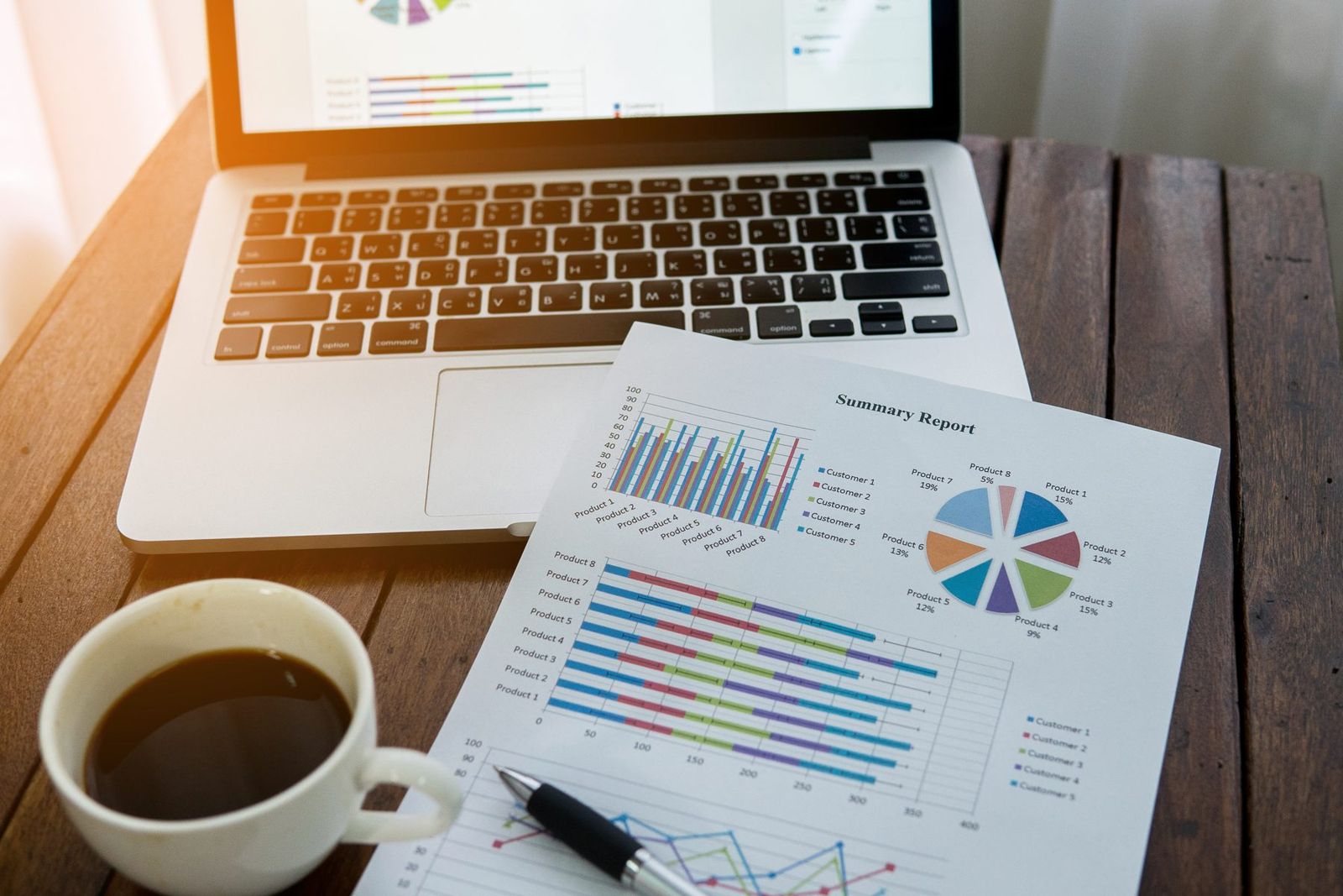 Un ordinateur portable, des graphiques imprimés et un café sur un bureau en bois