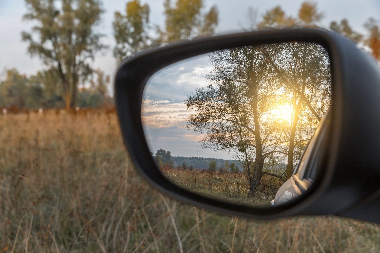 Un paysage au coucher du soleil vu dans le rétroviseur d'une voiture